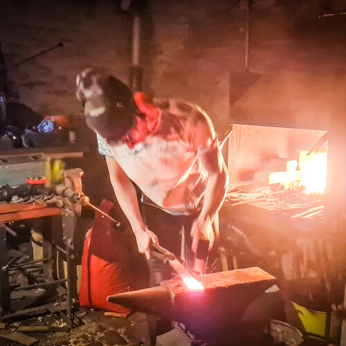 Vanessa Forch haut mit einem Schmiedehammer auf ein glühendes Stück Stahl um es zu schmieden. Dabei sprühen Funken.